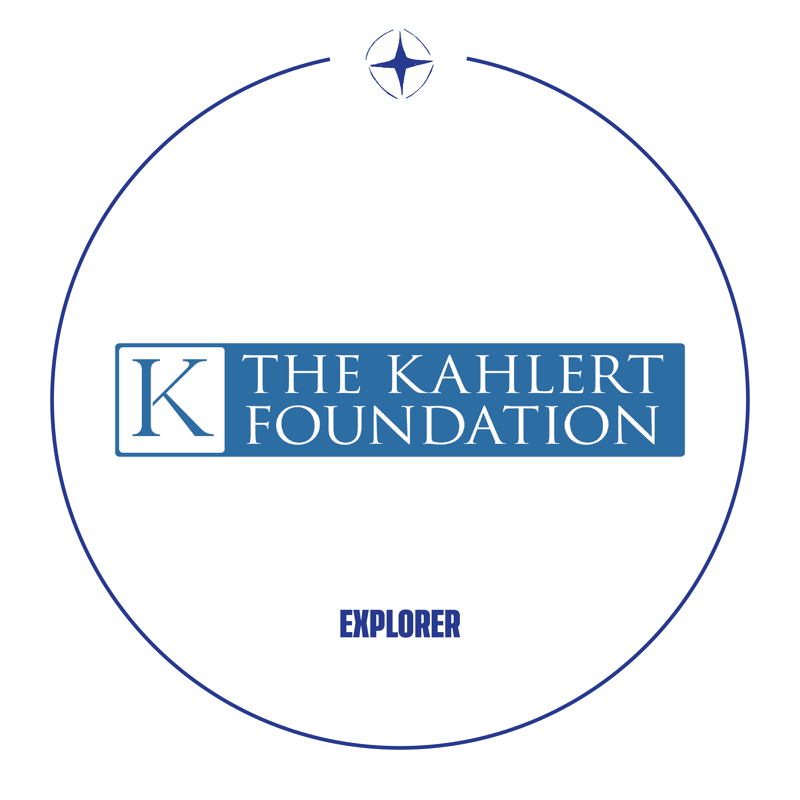This image shows the logo for "The Kahlert Foundation Explorer." The logo is circular with a compass rose at the top. Inside the circle, the foundation's name is displayed prominently in blue text, with a stylized "K" to the left. Below the name, the word "EXPLORER" is written in capital letters.