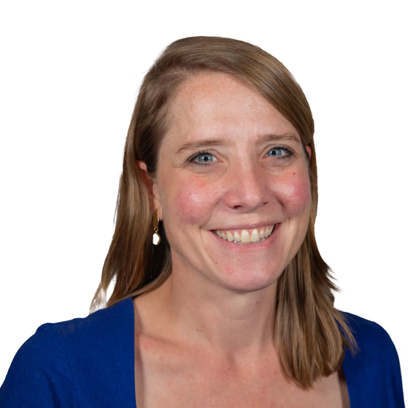 The image shows a woman with fair skin, light brown hair, and blue eyes. She is wearing a blue top and has a slight smile. The background is plain white, which makes the woman the focal point of the image. She appears to be looking directly at the camera.