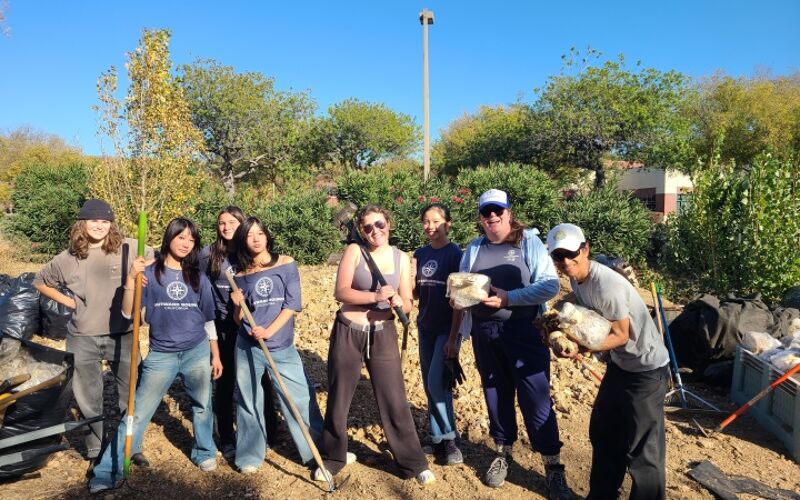 The image shows a group of people posing for a photo outdoors. They appear to be volunteers, possibly involved in a community project. Some are holding tools, and the background suggests a natural environment. The overall impression is one of teamwork and environmental engagement.