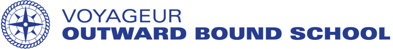 The image displays the logo of the Voyageur Outward Bound School. The logo features a circular design with a compass rose in the center, surrounded by a rope-like border. The school's name is written in a dark blue color below the circular design. The background is black.